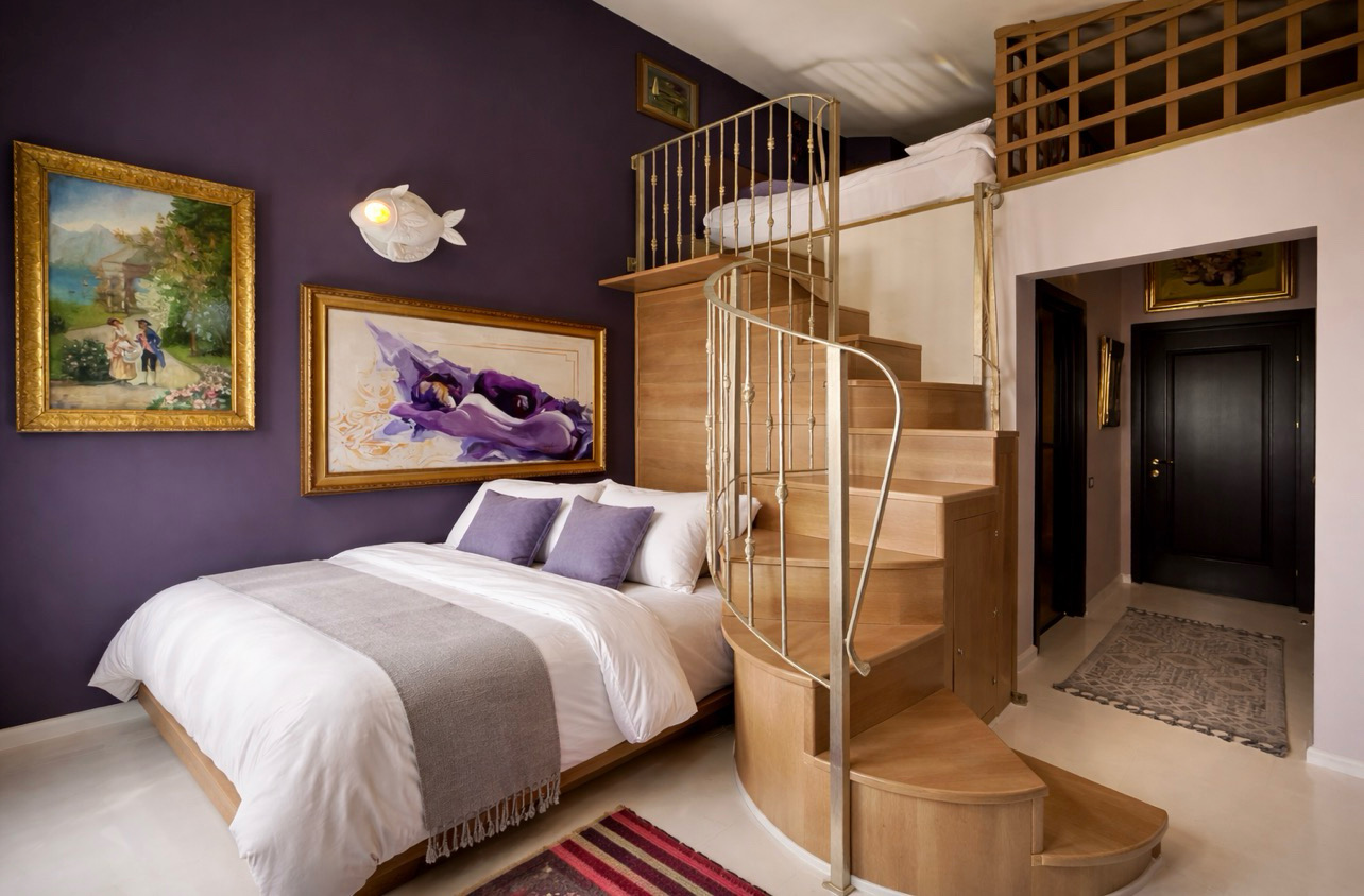 The French Loft with purple walls, a white bed and the staircase to the mezzanine